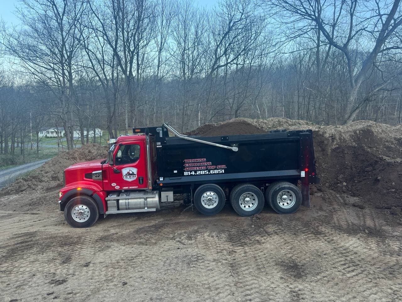 Branded EW Wise Freightliner dump truck backed up to a screened topsoil pile