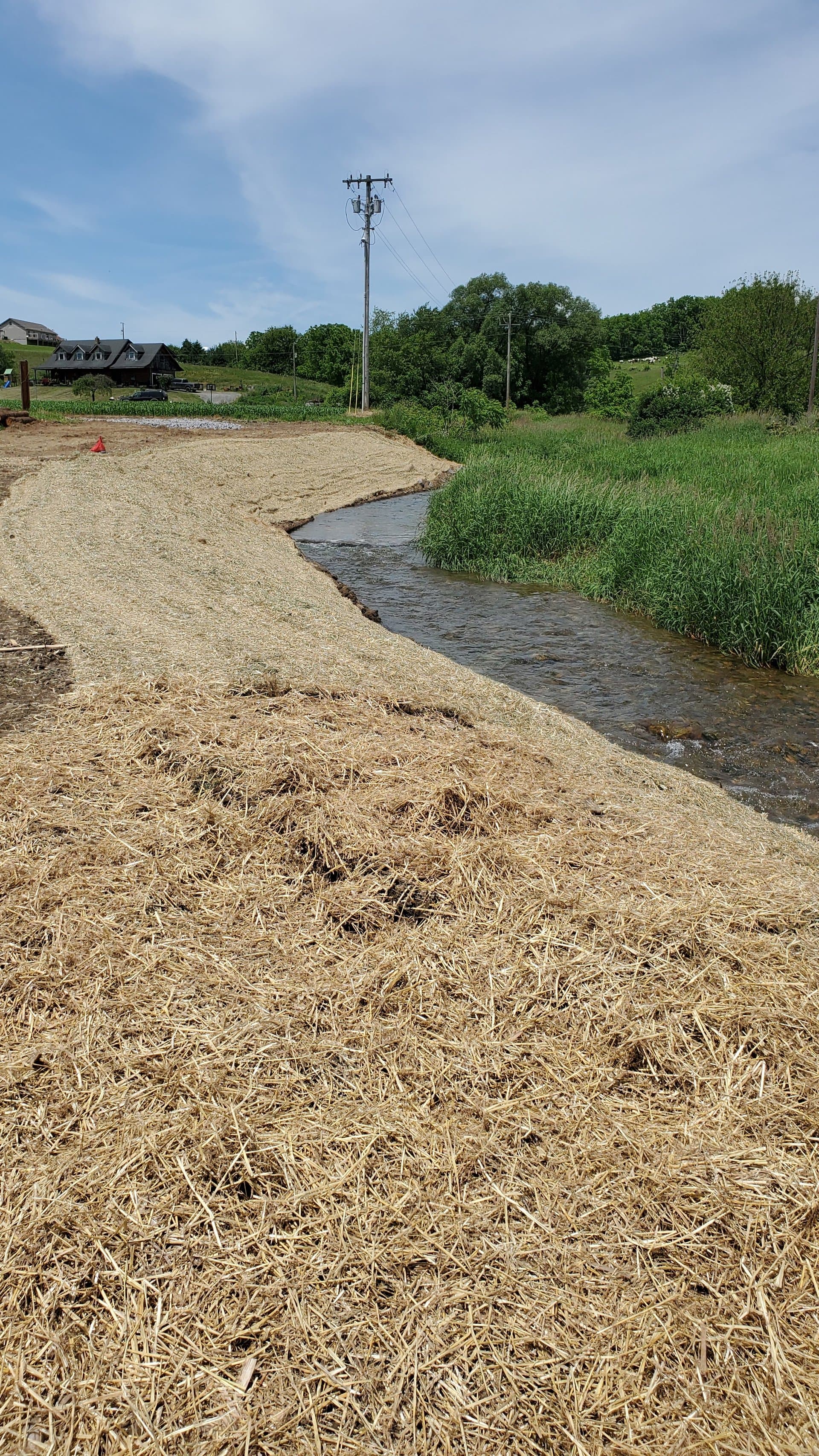 Finished curving streambank covered in straw mulch with farmhouse in the background