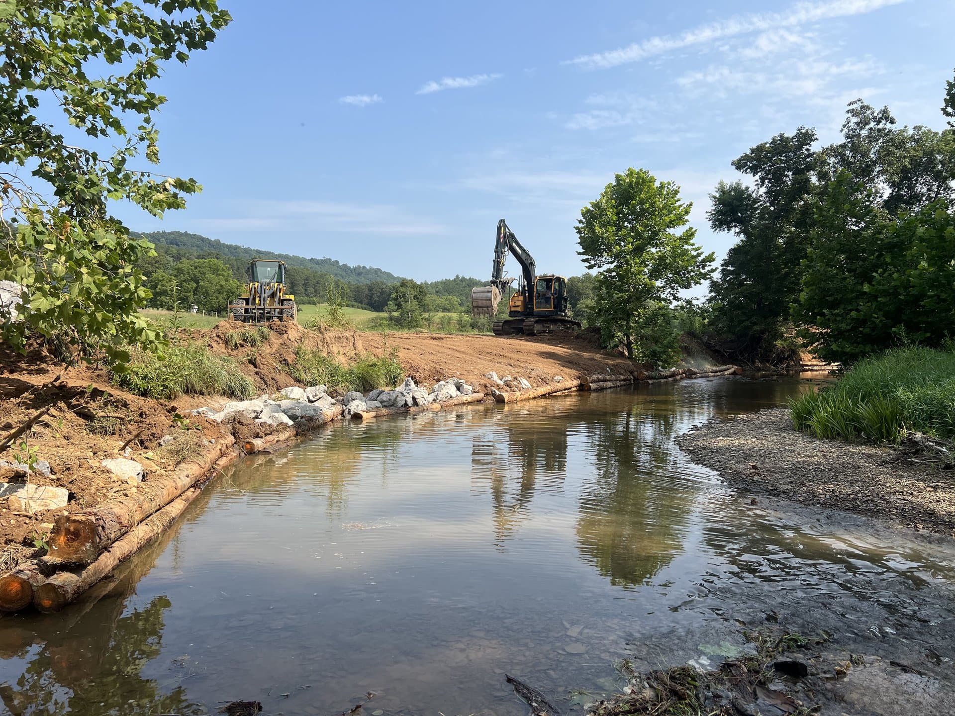 Hyundai excavator placing stone armor on a stream restoration project with mountains behind