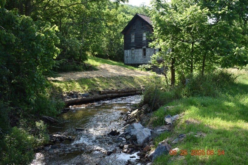 Old wooden building beside a restored creek with log toe stabilization