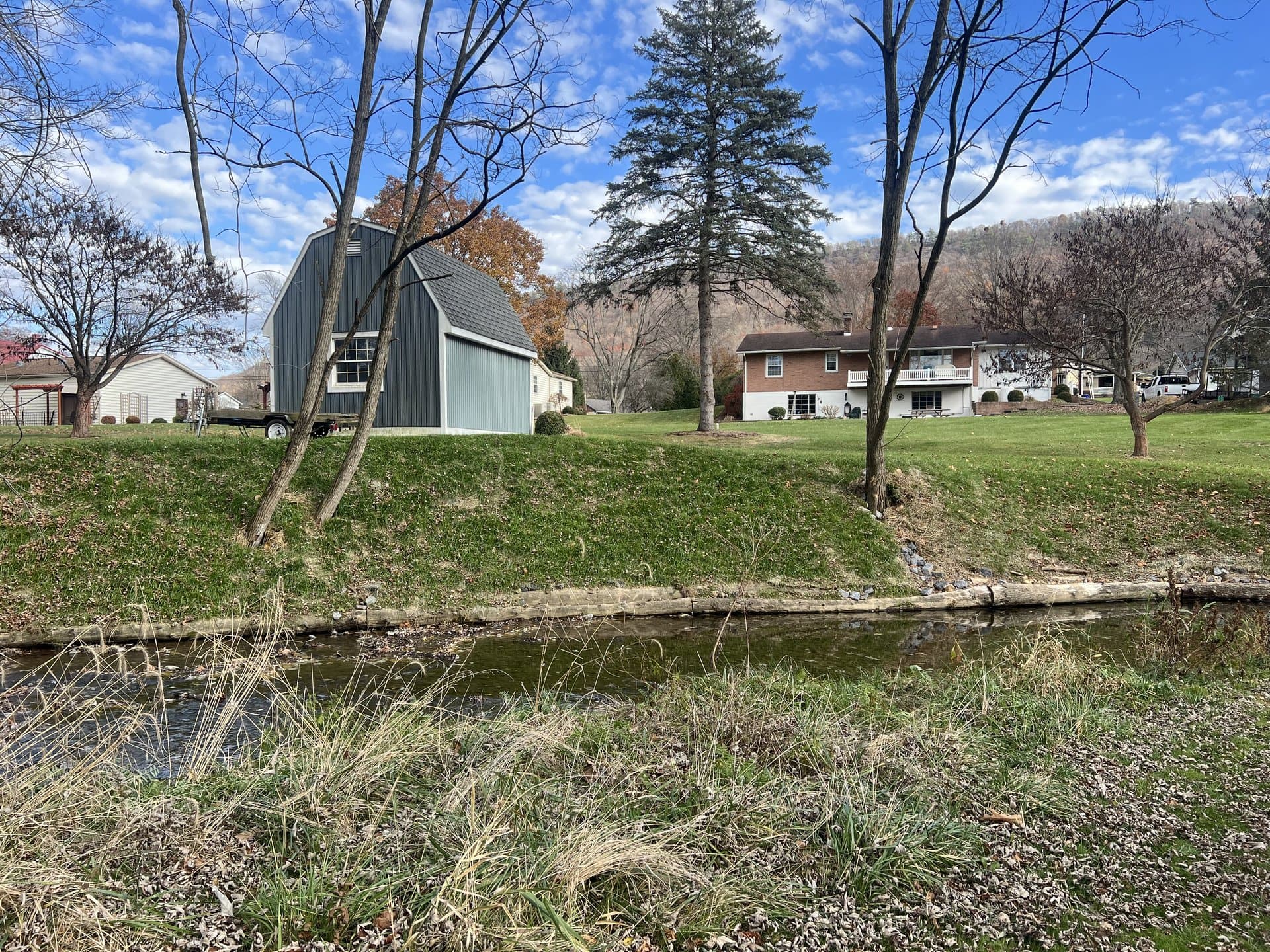 Restored stream running past a Pennsylvania property with barn and mountains in fall colors