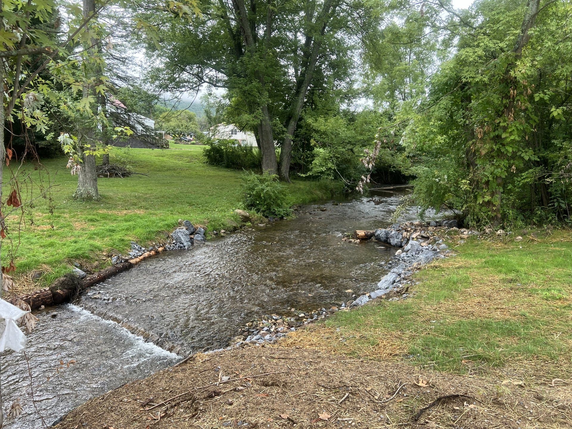 Restored stream with stone toe creating a pool and farmhouse in the background